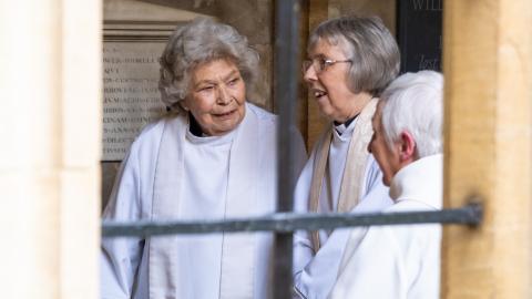 Three robed members of the 1994 cohort of women converse in the cloister.