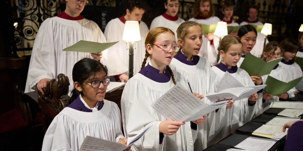 Frideswide Voices singing in the choir stalls, supported by the adult Clerks of the Cathedral choir. They are all in liturgical robes.