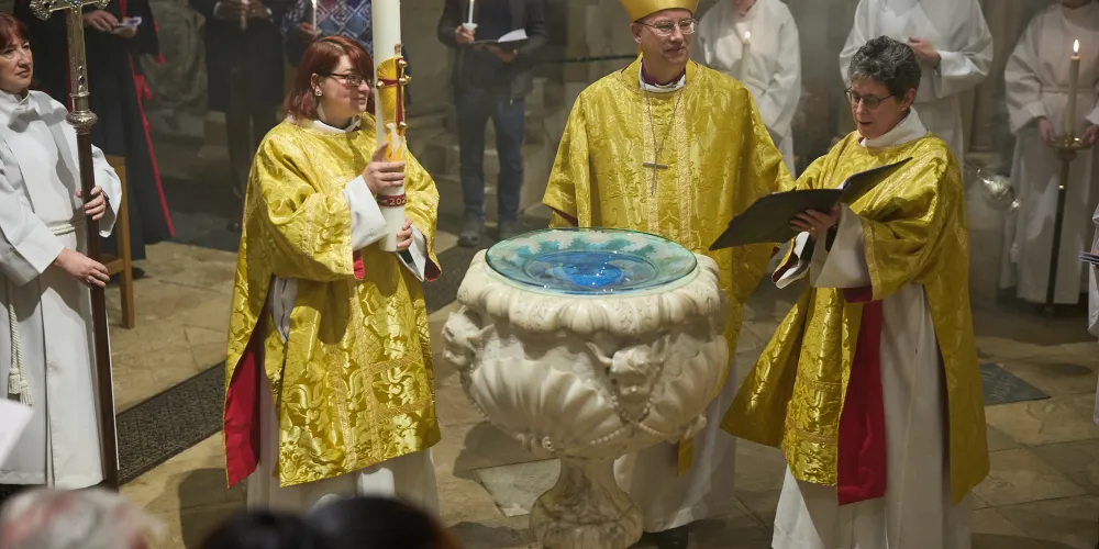 The Dean, Bishop of Oxford and Precentor around the font during the Easter Vigil Service with the congregation, prior to blessing the large paschal candle carried by the Precentor. The clergy are in robes and gold chasubles.