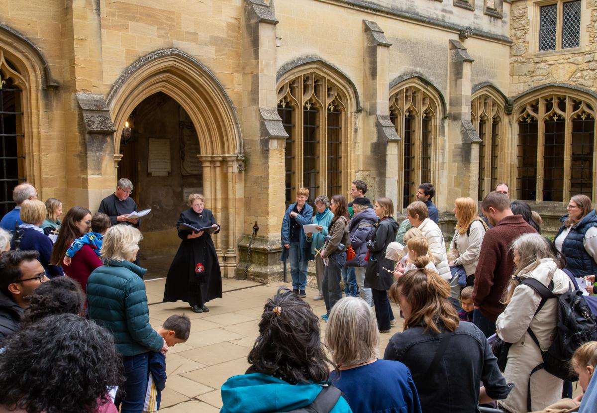 A group of children and their guardians stand in the middle of the cloisters as a robed verger reads to them during our Journey to bethlehem service in 2025