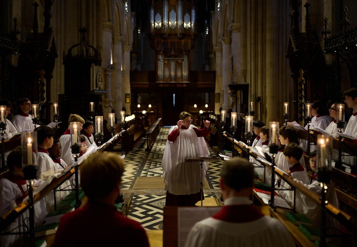 The 2025/26 Cathedral choir performing in an empty cathedral in the choir stalls. They are in their choir rorbes with lit candles