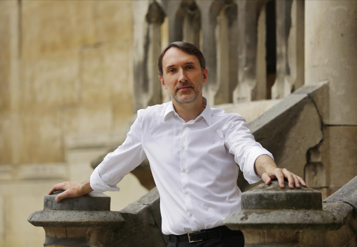 Organist Olivier Latry poses in a relaxed fashion in front of a medieval church.