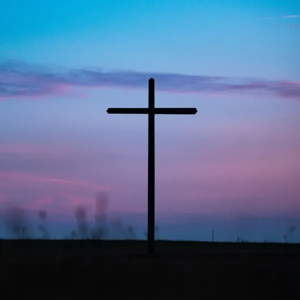 A distant Christian cross stands silhouetted against a darkening blue and pink sky in the final stages of twilight