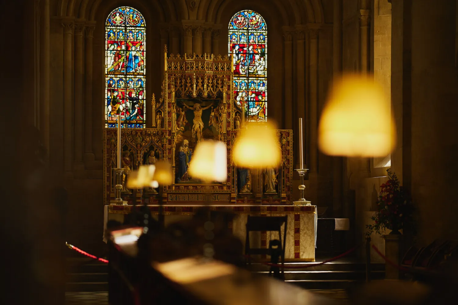 Lamps are lit in a dark cathedral, with the high altar in the background