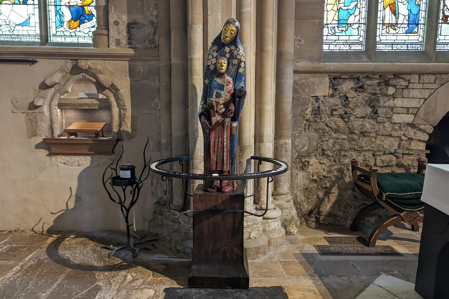 Peter Eugene Ball's sculpture 'Madonna', a statue of Mary with the child jesus at her feet, stands between the Bell and Lady chapel altars on a new, dark wood plinth. The plint is surrounded by a wrought iron circle of prickets for candles.