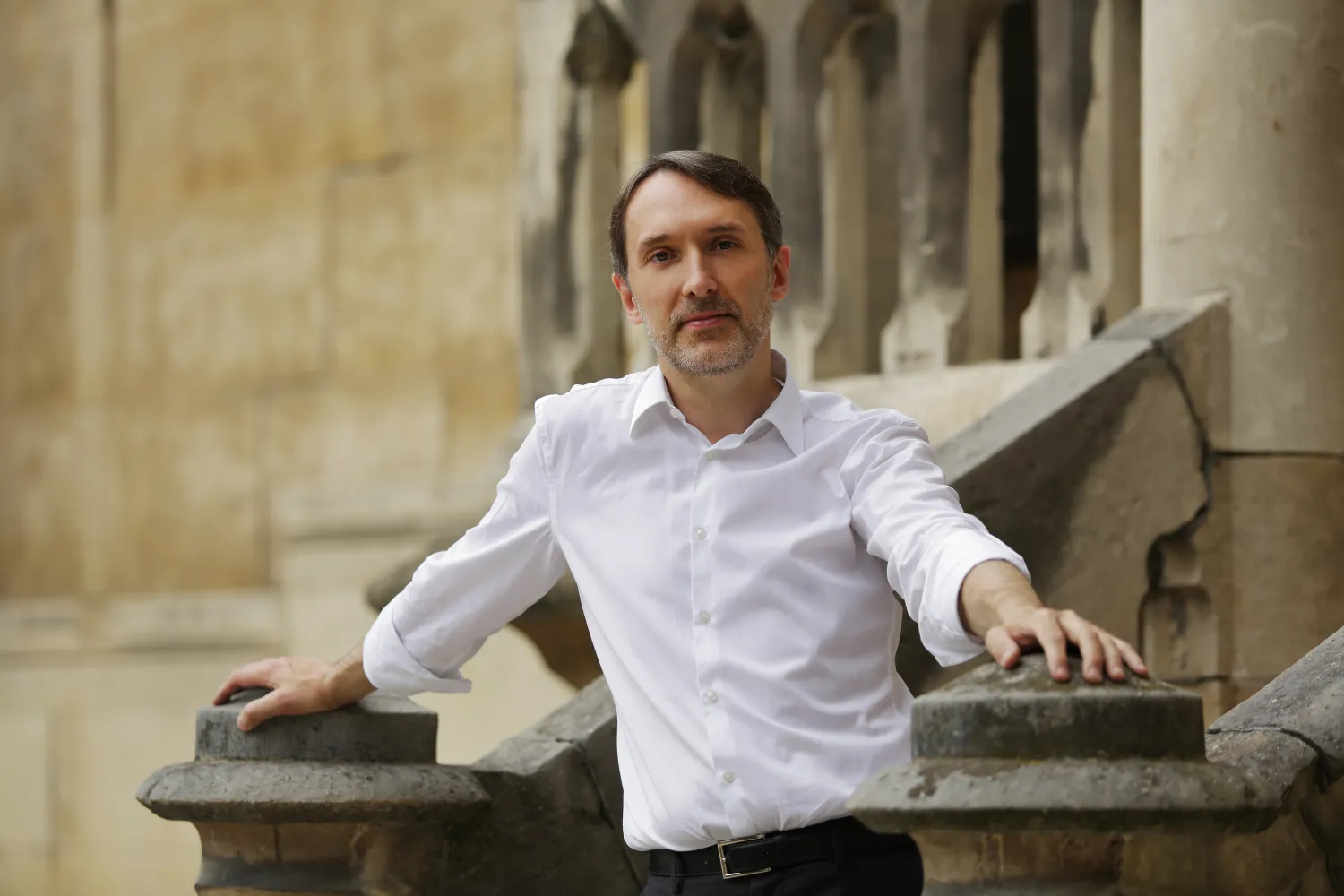Organist Olivier Latry poses in a relaxed fashion in front of a medieval church.