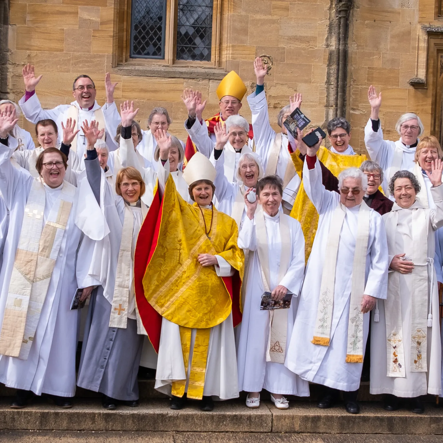 A large group of women ordained in 1994 are gathered wearing albs and stoles, and joined by Bishops Olivia Graham, Steven Croft and Gavin Collins. The first female Dean of Christ Church, Sarah Foot, is also present. They are waving and looking thrilled that women triumphed over discrimination to flourish in spirit and ministry.