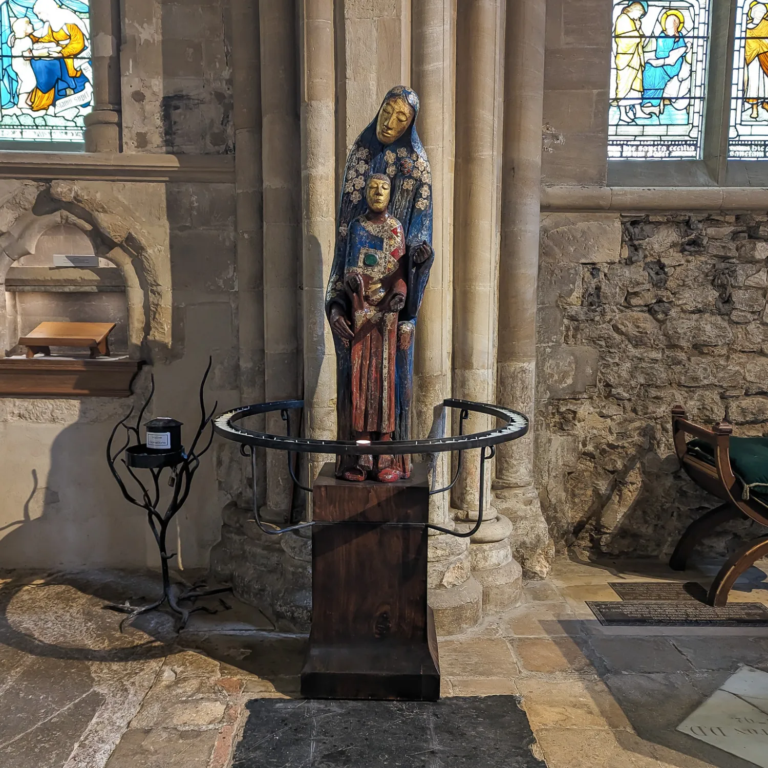 Peter Eugene Ball's sculpture 'Madonna', a statue of Mary with the child jesus at her feet, stands between the Bell and Lady chapel altars on a new, dark wood plinth. The plint is surrounded by a wrought iron circle of prickets for candles.